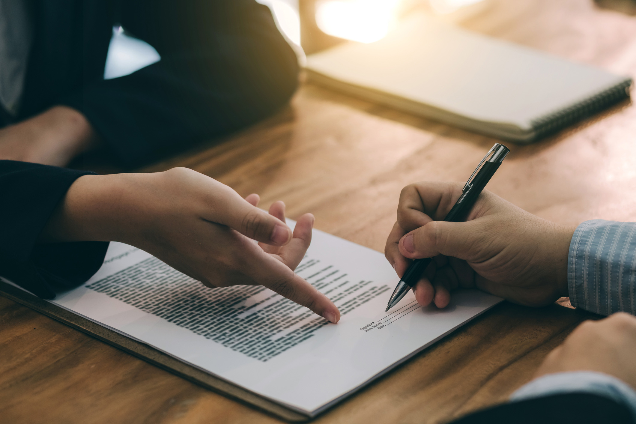 Two people at a desk, one pointing to a document as the other signs it