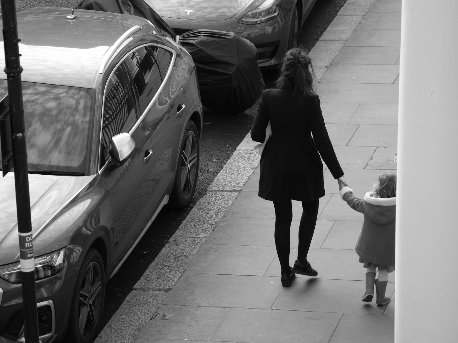 Woman holding child's hand walking on sidewalk
